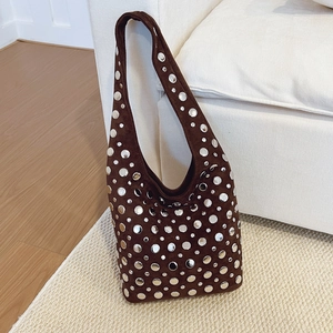 Dark brown suede hobo bag with silver rivets placed on a cozy white sofa backdrop