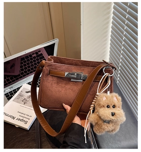 Detailed close-up of brown suede kelly bag featuring a metal buckle and plush dog charm