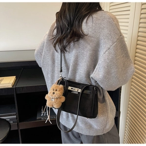 Detail of minimalist black shoulder bag with silver turn-lock and cute bear pendant