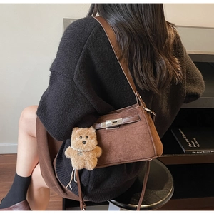 Detail of dark brown suede Kelly bag featuring silver twist lock and plush bear charm