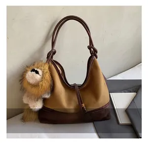 Detail of a brown suede tote bag with leather straps and a plush lion charm