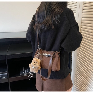 Close-up of brown suede Kelly bag with metallic lock and cute plush bear charm detail