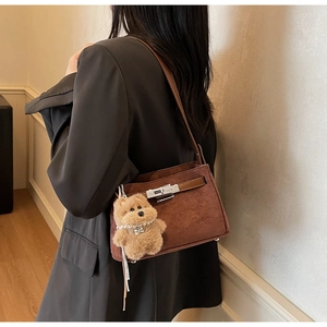 Close-up of brown suede underarm bag with silver lock and plush bear charm detail