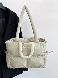 Beige quilted nylon tote bag with dual handles and puffy design against a white wall