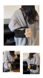 Detail of matte black crossbody bag with brown plush bear charm on grey knit sweater
