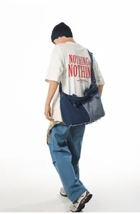 Detail of a large denim patchwork messenger bag with distressed frayed edges on a model