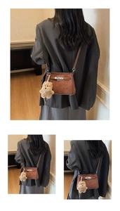 Detail of brown suede crossbody bag featuring metal buckle and plush bear pendant accessory