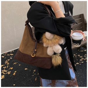 Detail of suede patchwork tote bag with gold hardware and plush doll pendant in autumn style