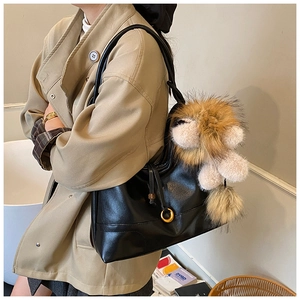 Detail of black glossy tote bag with oversized brown plush lion charm for stylish commuting