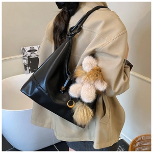 Close-up of black hobo bag featuring knotted shoulder strap and plush animal charm detail