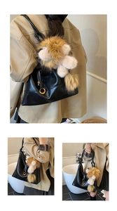 Detail of black faux suede tote bag featuring a plush lion charm and gold ring hardware
