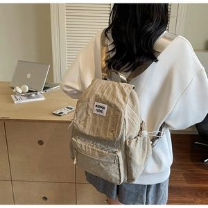 Close-up of khaki pleated nylon backpack with branding label and side drawstring pocket