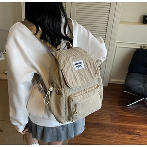 Close-up of beige crinkled nylon backpack featuring waswac rules woven label and zipper pocket