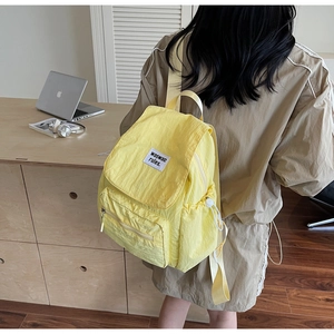 Detail of a bright yellow nylon backpack featuring a waswac rules woven label and side pocket