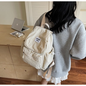 Cream nylon backpack with flap cover and front zipper pocket on a minimalist desk set