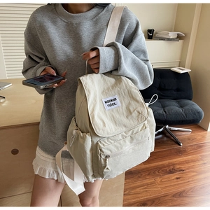 Close-up of beige nylon backpack featuring a brand label and sleek drawstring pockets