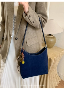 Détail du sac hobo en daim bleu foncé avec un pendentif souriant et un charme de cœur