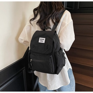 Detail of black waterproof nylon backpack with white text patch on wooden stairs
