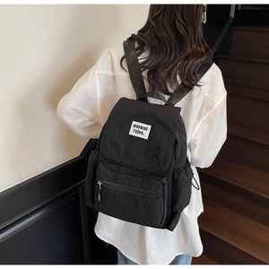 Rear view of a minimalist black nylon backpack with flap closure and white woven label