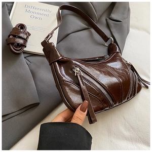 Detail of dark brown glossy patent leather bag with fringe zippers and dual straps