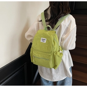 Detail of light green nylon backpack with flap cover and side drawstring pocket on model