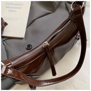 Close-up of deep brown glossy patent leather bag with silver zipper on grey blazer