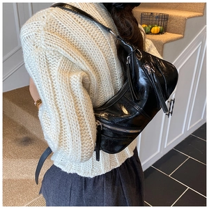 Adjustable black shiny leather hobo bag with zipper details worn as a crossbody bag