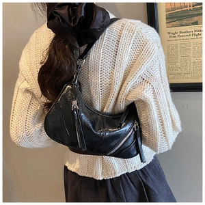 Close-up of a black glossy shoulder bag with multiple zippers worn over a beige sweater