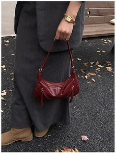 Detail of dark red patent leather shoulder bag with tassels in a retro urban setting
