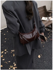 Detail of burgundy crescent bag with silver zippers styled on a grey wool coat