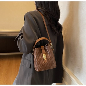 Brown woven bucket bag featuring a gold metal clasp and a stylish circular top handle