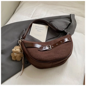 Detail view of brown suede crescent bag with leather straps and plush bear charm