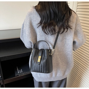 Detail of woven texture and gold twist lock on black bucket bag with top handle