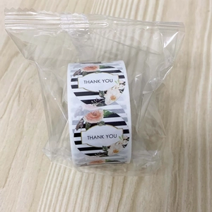 Close-up of roll thank you stickers in polybag on wooden desk with floral pattern