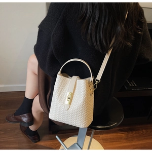 Detailed view of white woven bucket bag with gold hardware and adjustable strap