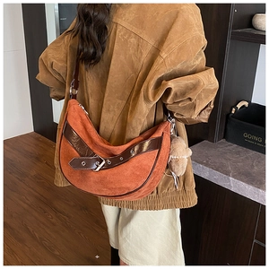 Detail of a large orange suede hobo bag with patent leather strap and bear charm