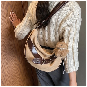 Detail view of khaki half-moon crossbody bag with leather buckle and plush bear charm