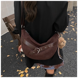 Detail of a dark brown suede crescent bag with a leather strap and a plush bear charm