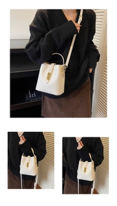 Detail of white woven bucket bag with gold metal lock and adjustable shoulder strap