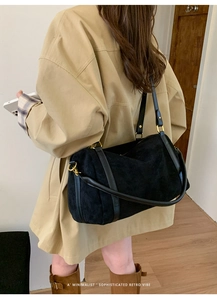 Sac Boston en daim noir avec détails dorés porté par un mannequin en trench-coat beige