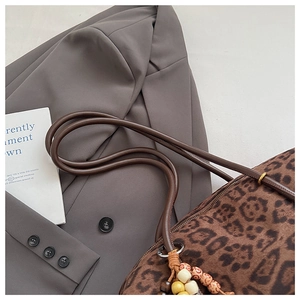 Detail view of leopard print tote bag with beaded pendant on a neutral blazer