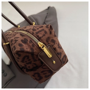 Detail of leopard print handbag featuring golden metal zipper and brown leather trim