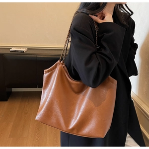 Detail of a brown leather tote bag with a metallic chain and leather shoulder strap