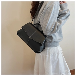 Detailed side view of a black pebbled faux leather crossbody bag with white stitching