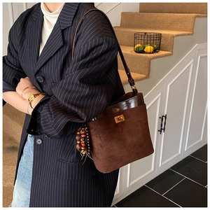 Detail of dark brown suede bucket bag featuring golden twist lock and beaded tassel charm