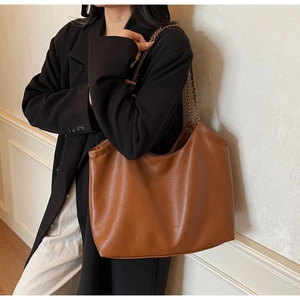 Detailed texture of brown faux leather tote bag with metal chain strap and embossed logo