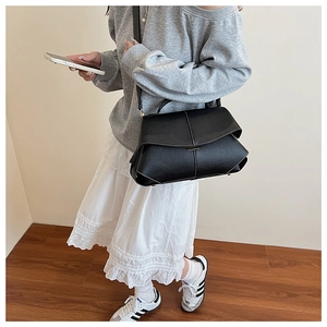 Detail of black crossbody bag featuring contrast white stitching and metal bar clasp