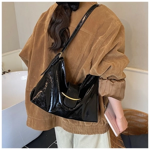 Detail of black glossy leather shoulder bag featuring a crescent gold metallic buckle