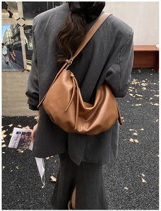 Detail of caramel faux leather hobo bag with knotted strap on model in gray suit