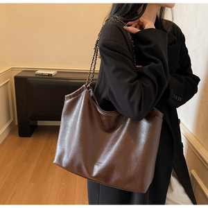 Detail of dark brown tote bag with metal chain strap and embossed logo texture